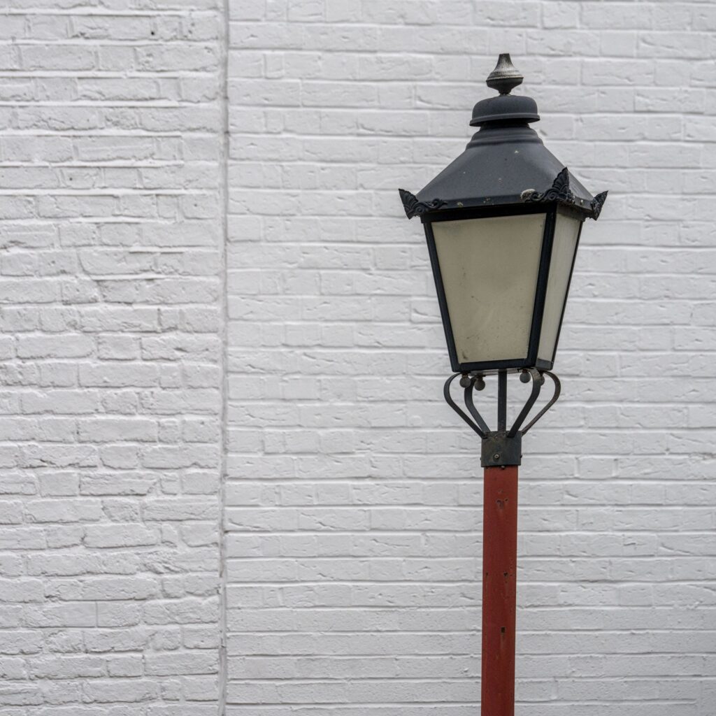 Simple formalist composition of lamp post against white brick wall